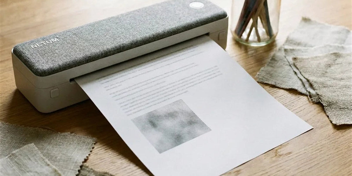 Imprimante thermique A4 au dessus gris façon tissu qui sort une page nettement imprimée, sur une table d'atelier en bois
