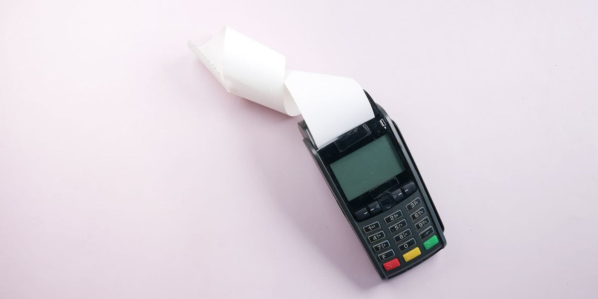 Terminal de paiement qui imprime un ticket sur papier thermique, sur fond rose