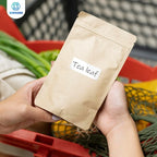 Mains tenant un sachet kraft portant une étiquette manuscrite Tea leaf, devant un cageot de légumes