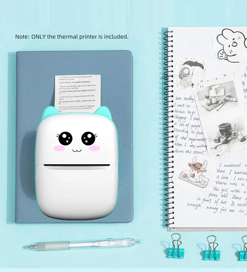 Imprimante à oreilles menthe posée sur un carnet bleu, imprimant un texte, à côté d'un carnet à spirale illustré et d'un stylo