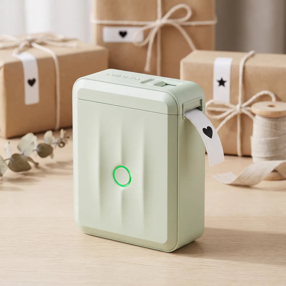 Étiquette cœur qui sort de l'imprimante NIIMBOT D110M vert sauge, paquets cadeaux en kraft étiquetés derrière